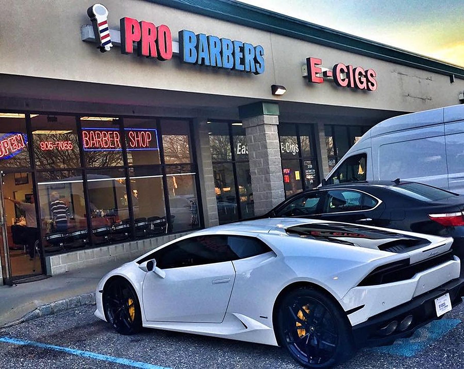 The Pro Barbers storefront on Route 9 with its red and blue sign, neon Open sign in the window, and a white Lamborghini parked out front.